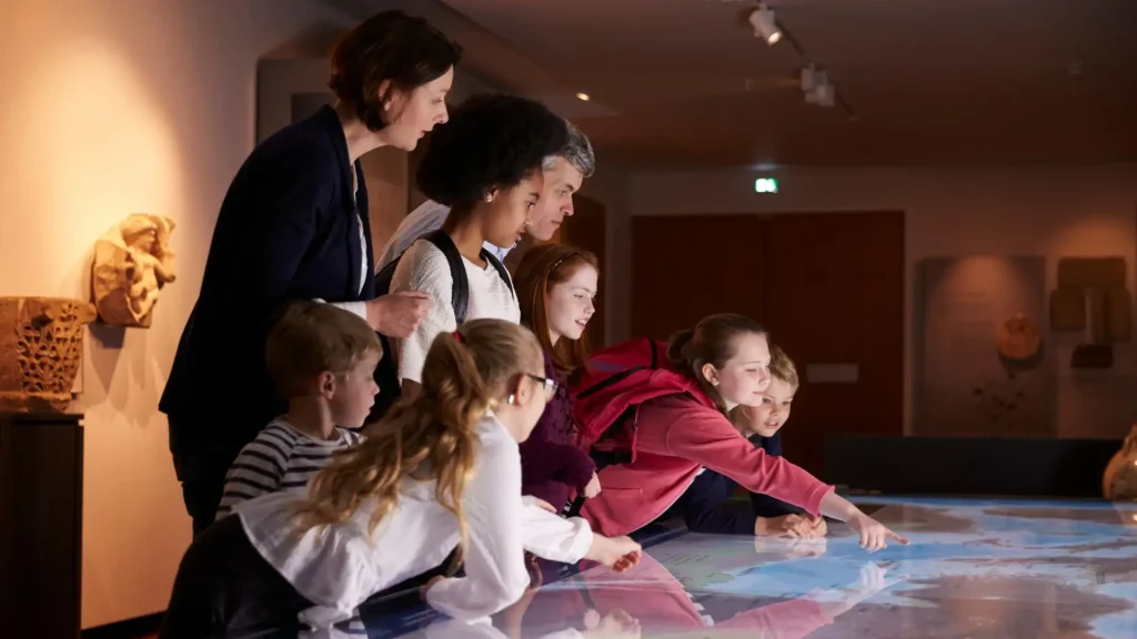 Eine Gruppe von Kindern und Erwachsenen schauen sich gemeinsam Informationen auf einem interaktiven Bildschirm an.